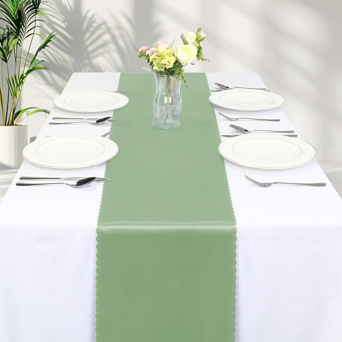 Sage green satin table runner centered on a dining table with white plates