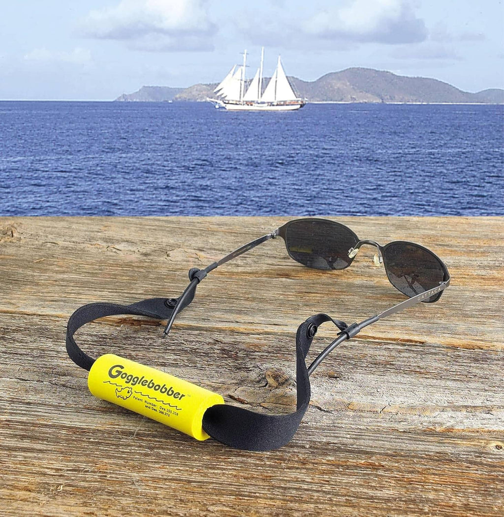 Floating sunglass retainer strap on wooden surface with black band and yellow foam