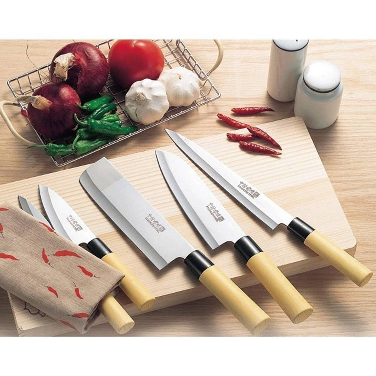 5 Japanese kitchen knives on a cutting board with vegetables in the background