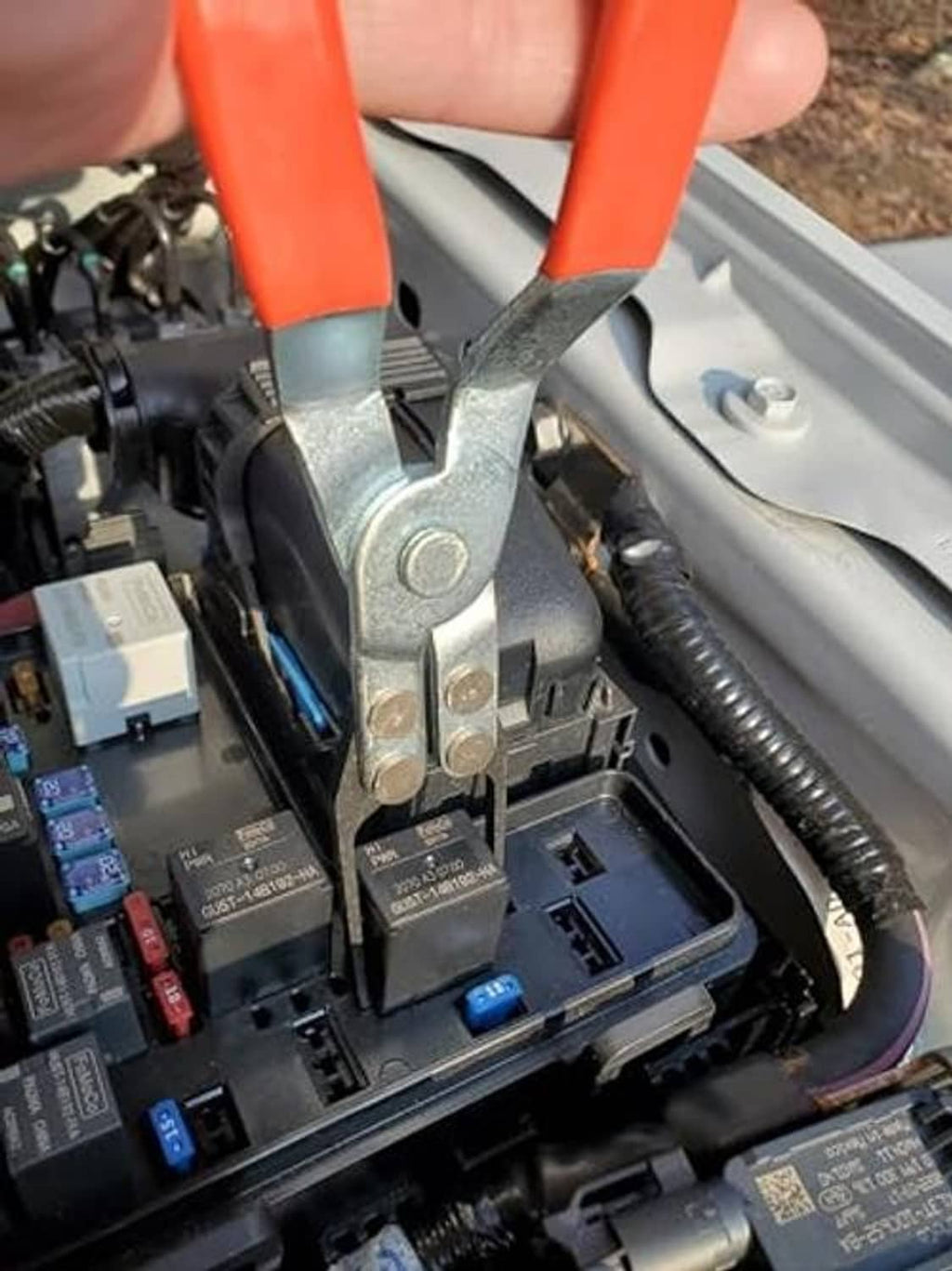 Relay puller removing a relay from an automotive fuse box socket.