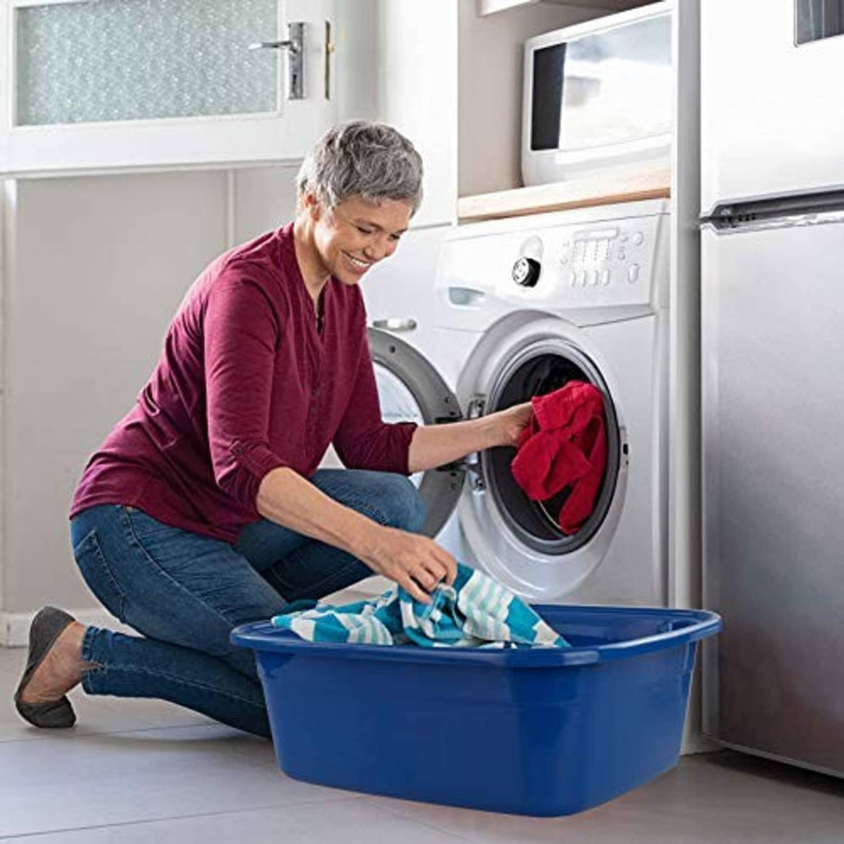 Blue plastic washing basin on the floor with laundry inside near a washer