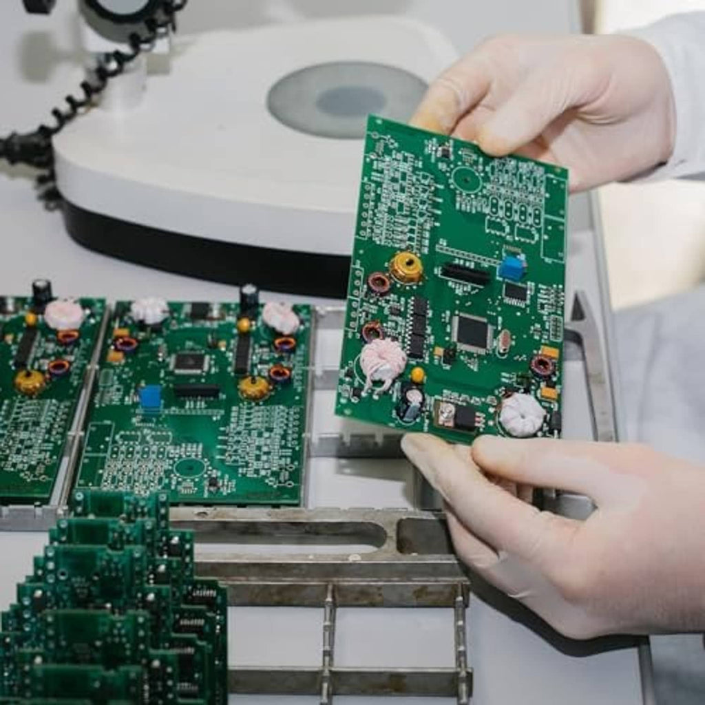 Technician holding a green circuit board during electronics assembly