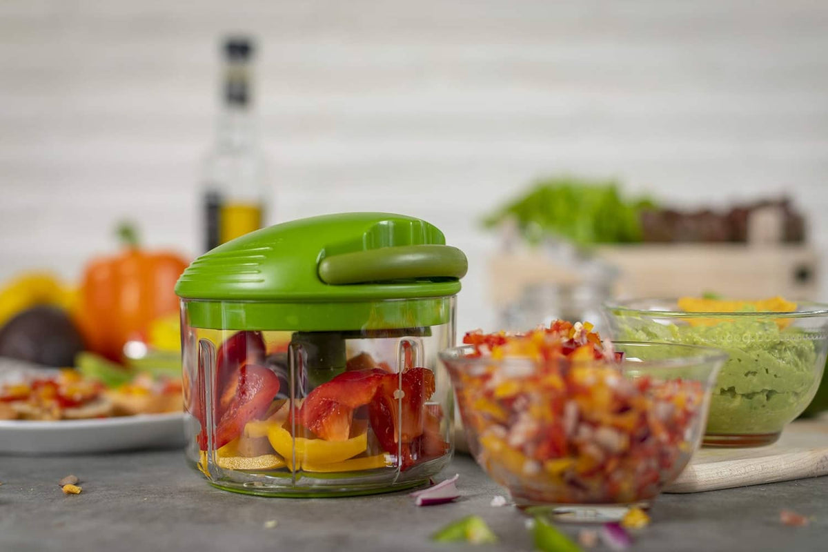 Green pull-cord chopper with clear container filled with chopped fruit on table