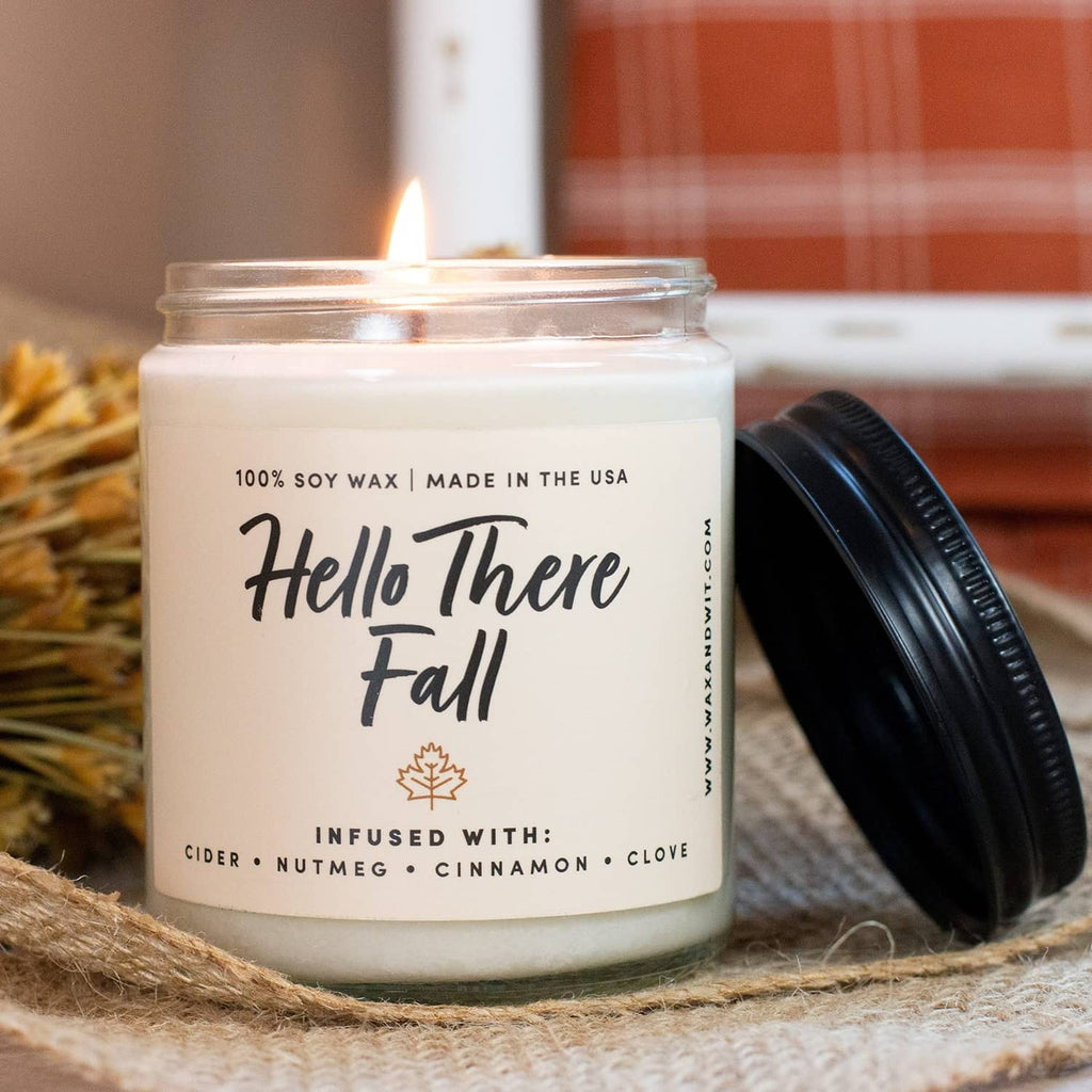 Scented soy candle jar with 'Hello There Fall' label and black lid set beside it