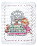 White baby quilt with multicolor stamped cross-stitch scene of a girl, bunny, and basket