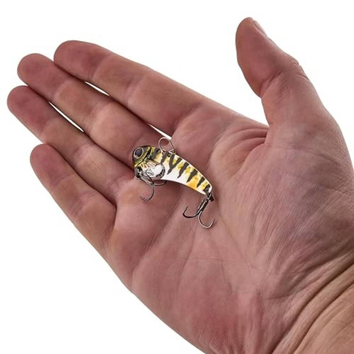 Blade bait fishing lure in hand, yellow-and-green pattern with two treble hooks