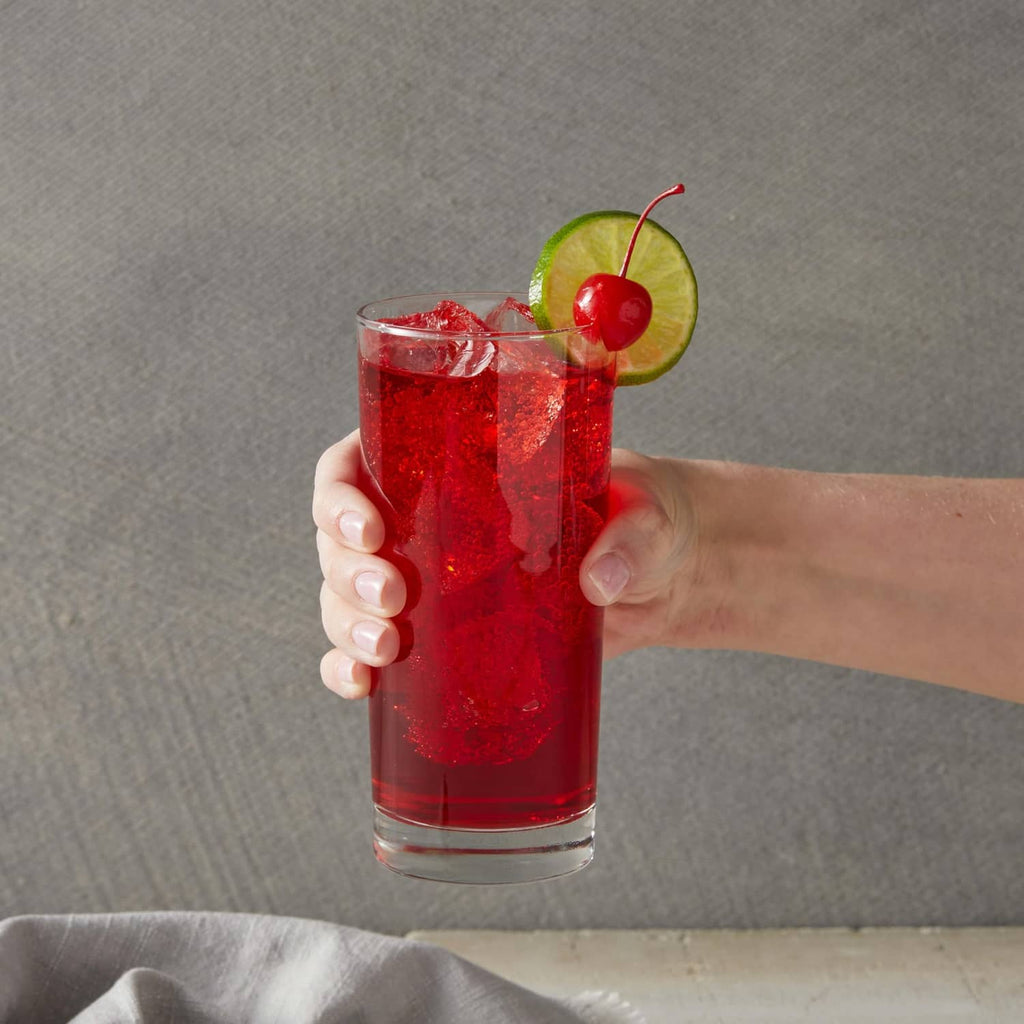 Hand holding a red cherry syrup drink with lime slice and cherry garnish