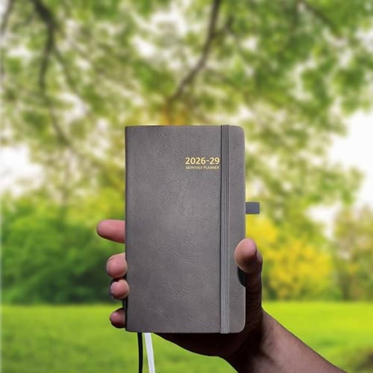 Gray pocket planner held in hand outdoors with elastic strap visible