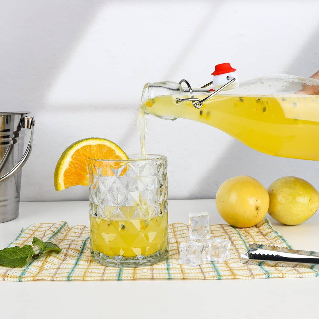 Clear glass swing-top bottle with red flip cap, filled with yellow drink and droplets