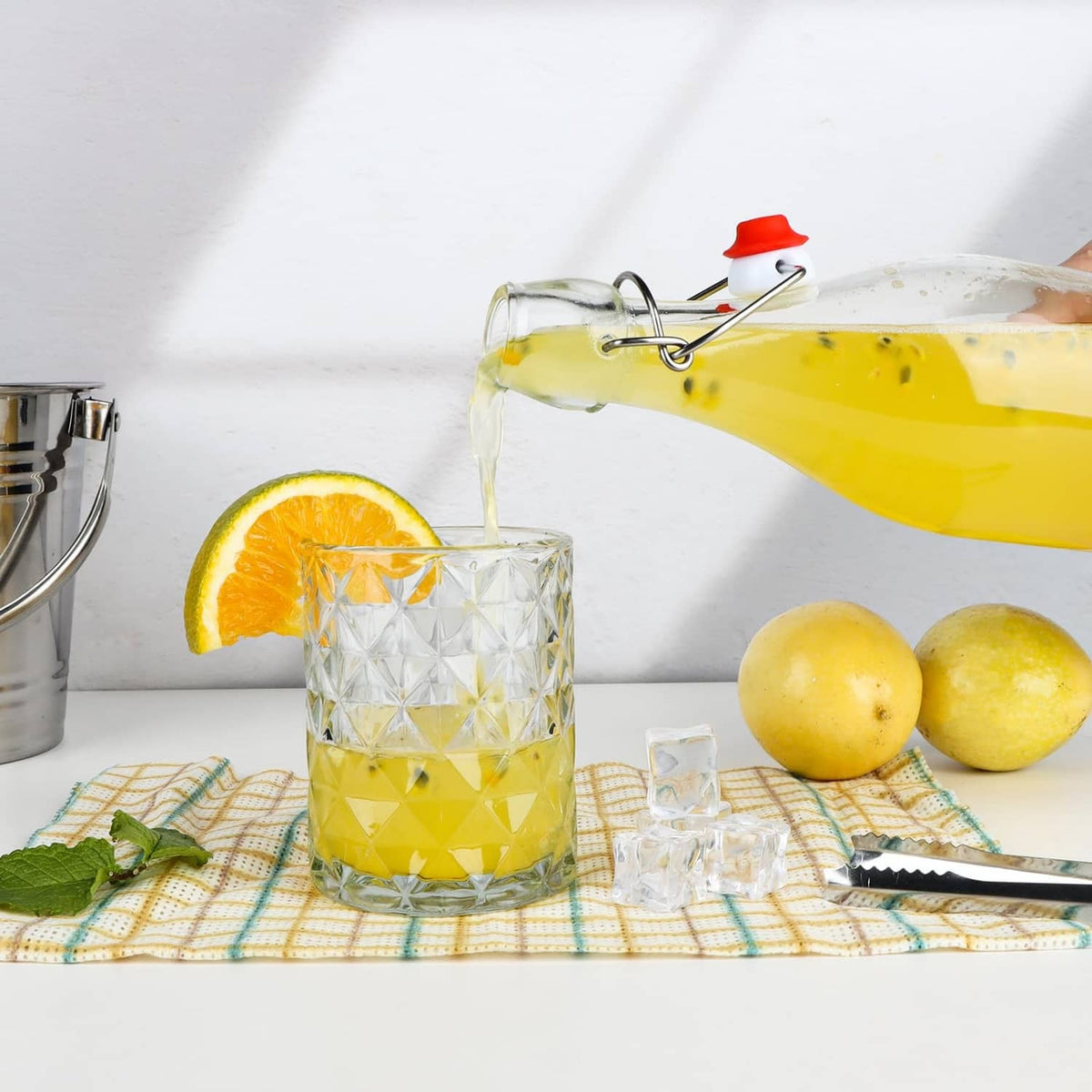 Clear glass swing-top bottle with red flip cap, filled with yellow drink and droplets