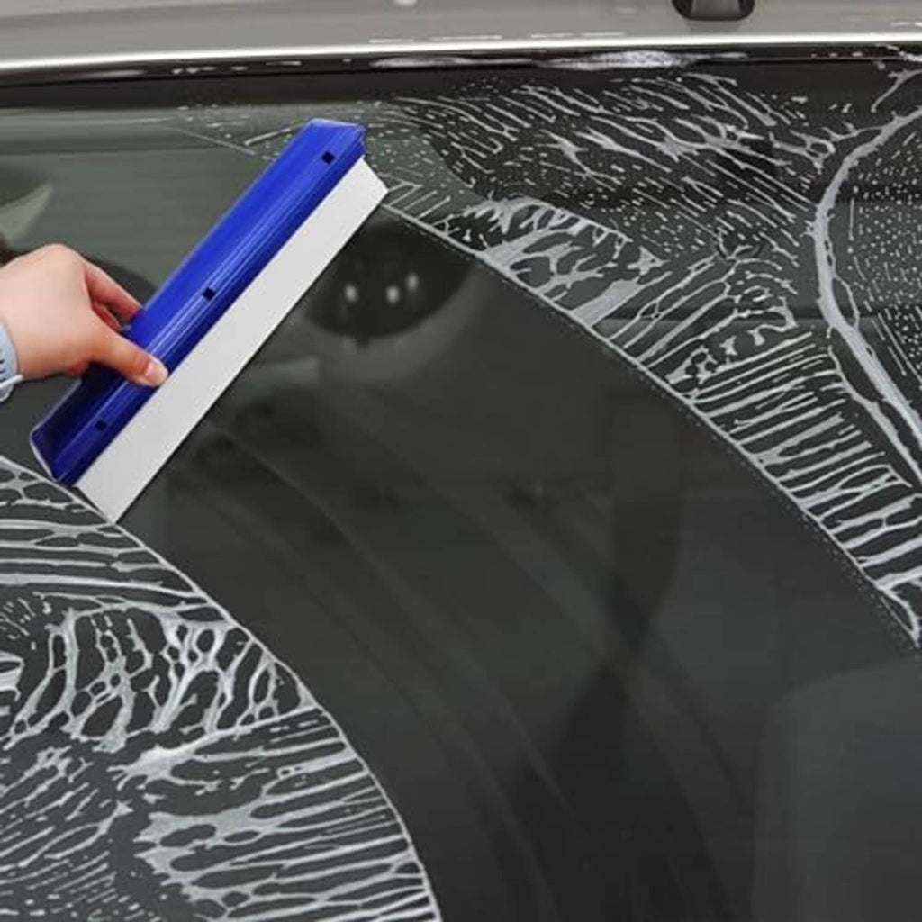 Hand using a blue-and-white car window squeegee water blade on wet glass