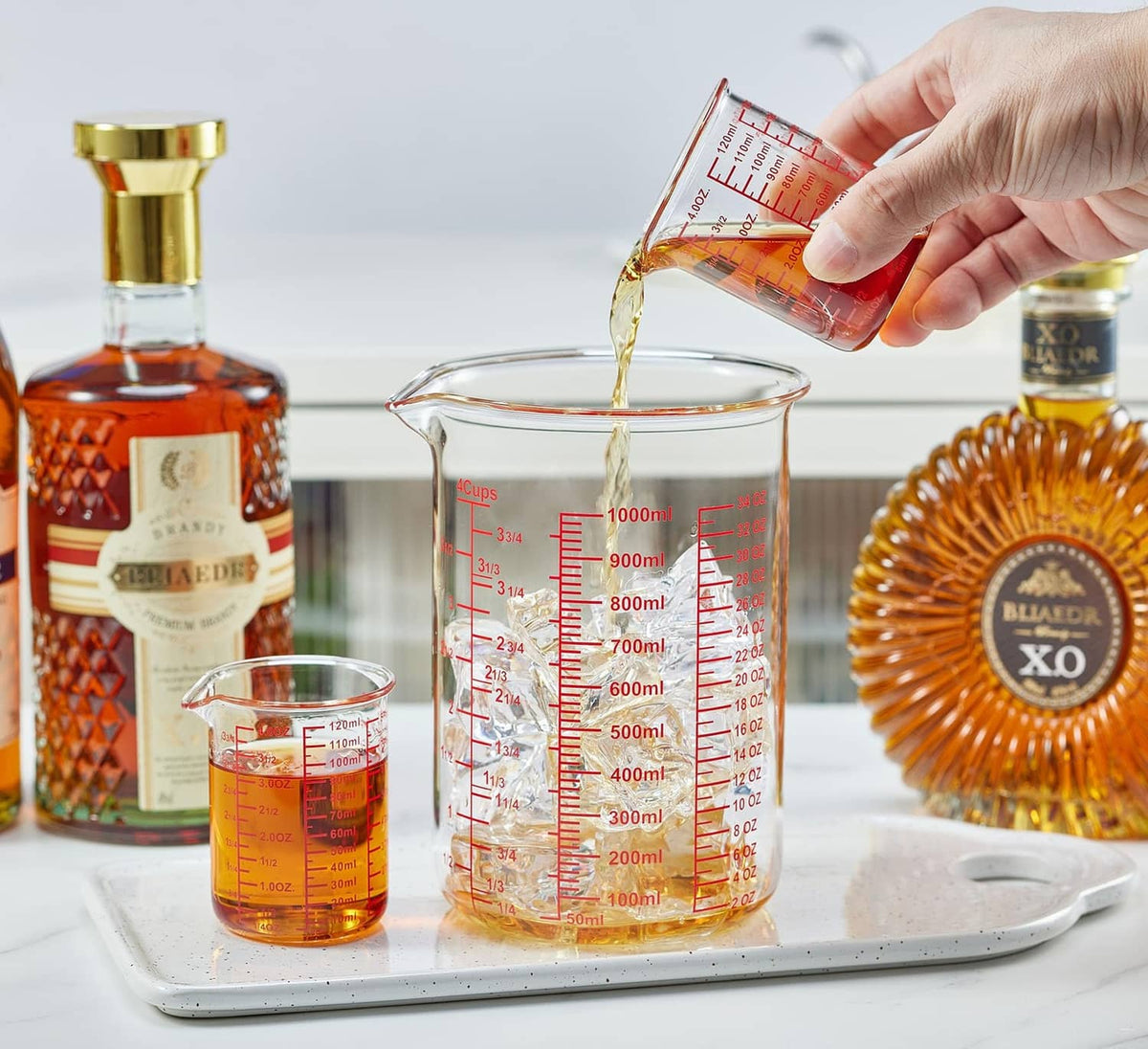 Clear glass measuring cup with red scale markings, pouring liquid into larger jug.