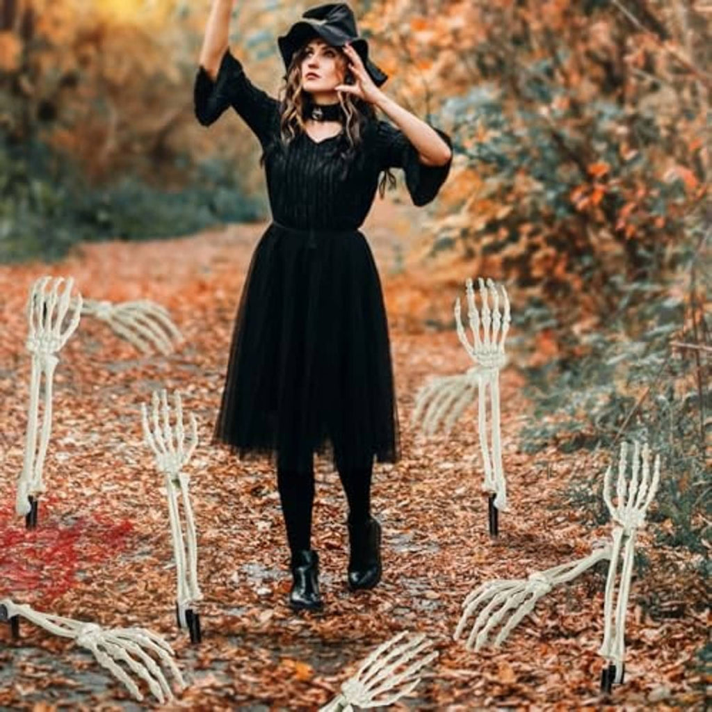 White skeleton hand stakes around a person in a black witch dress outdoors