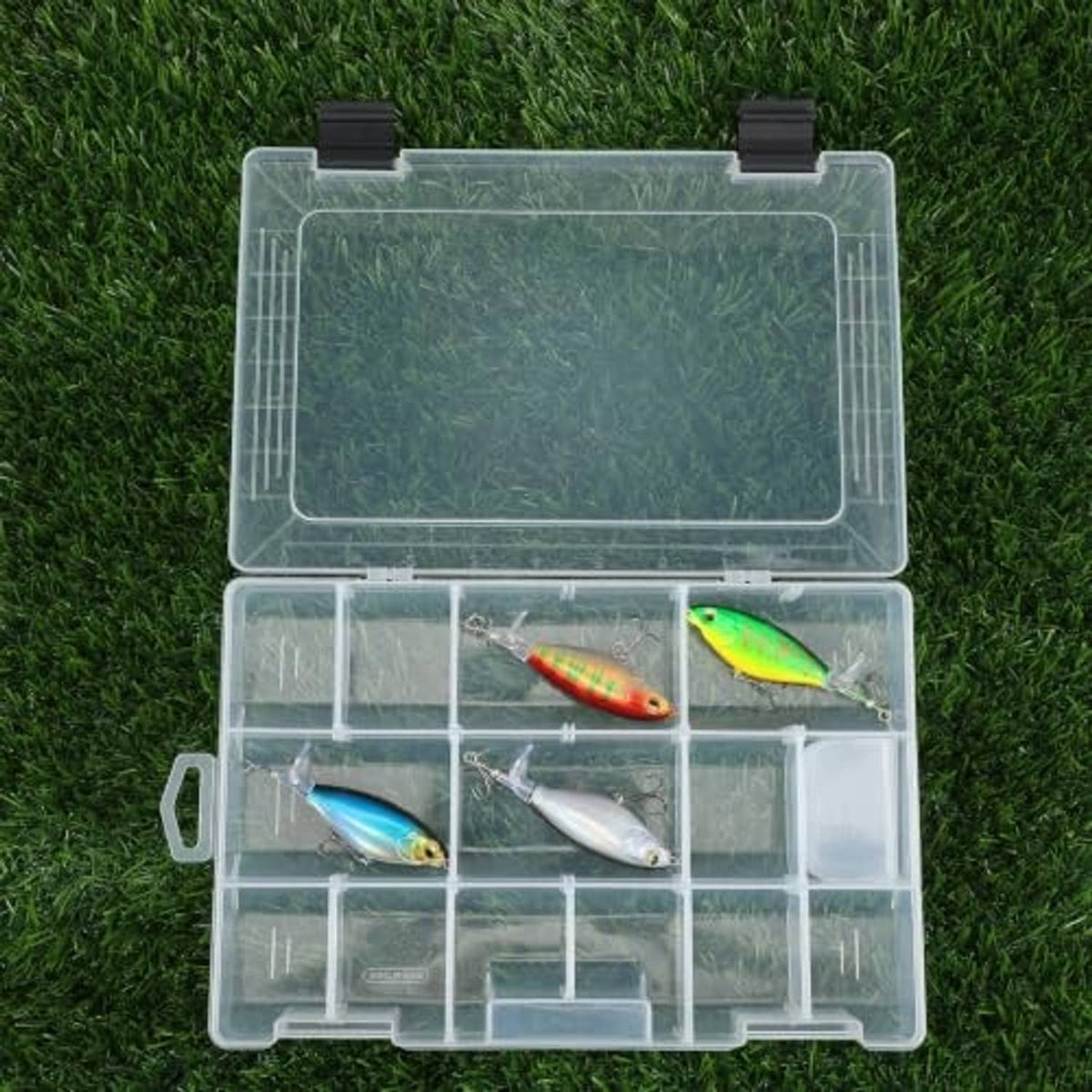 Clear tackle box on grass with lures stored across divided compartments
