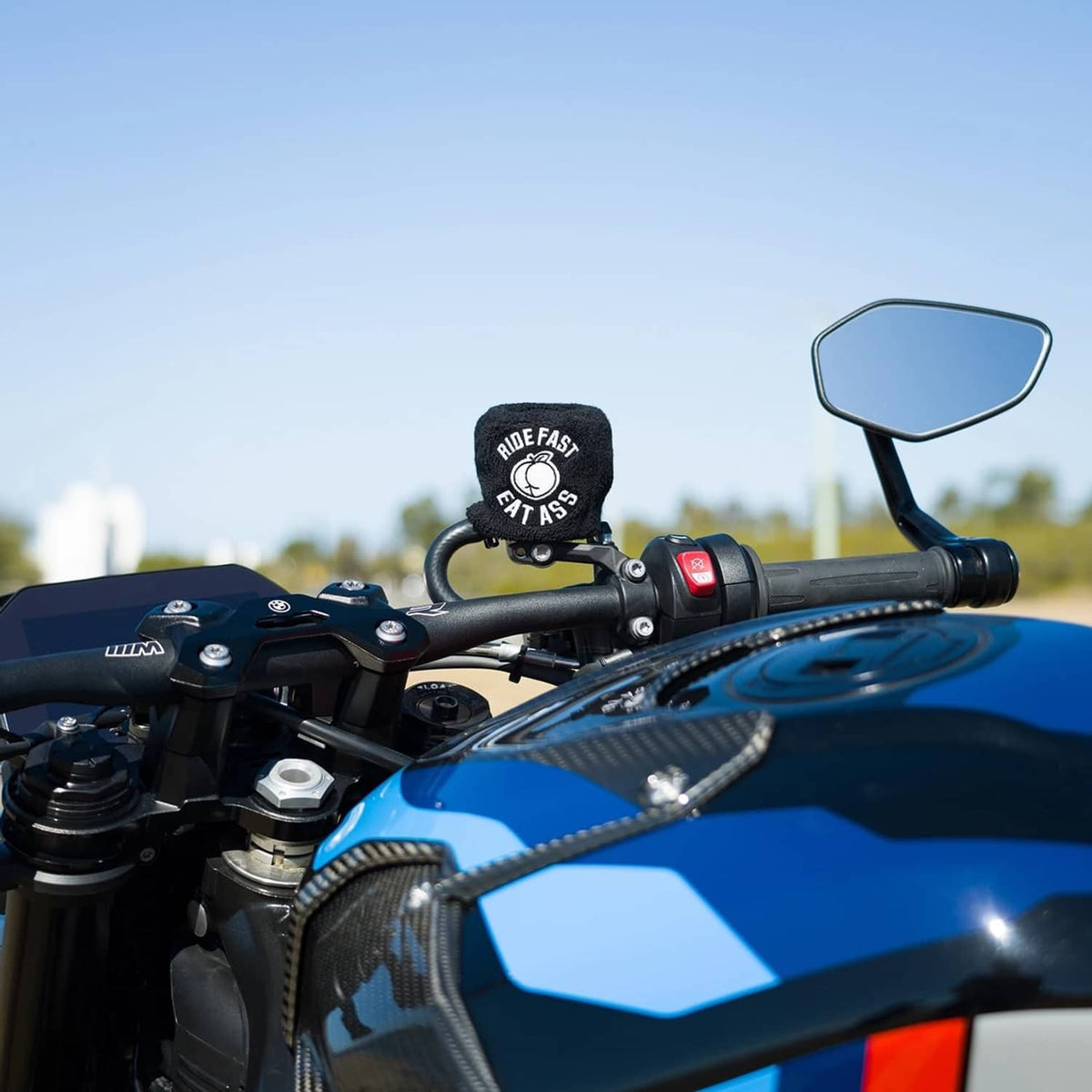 Black brake fluid reservoir cover sock with “RIDE FAST EAT ASS” logo near handlebar controls