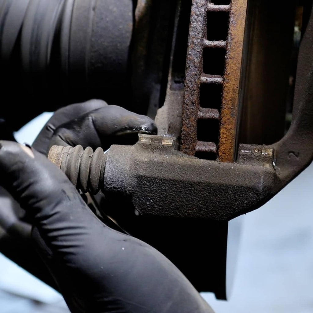 Brake caliper component with gloved hand applying lubricant to metal surface