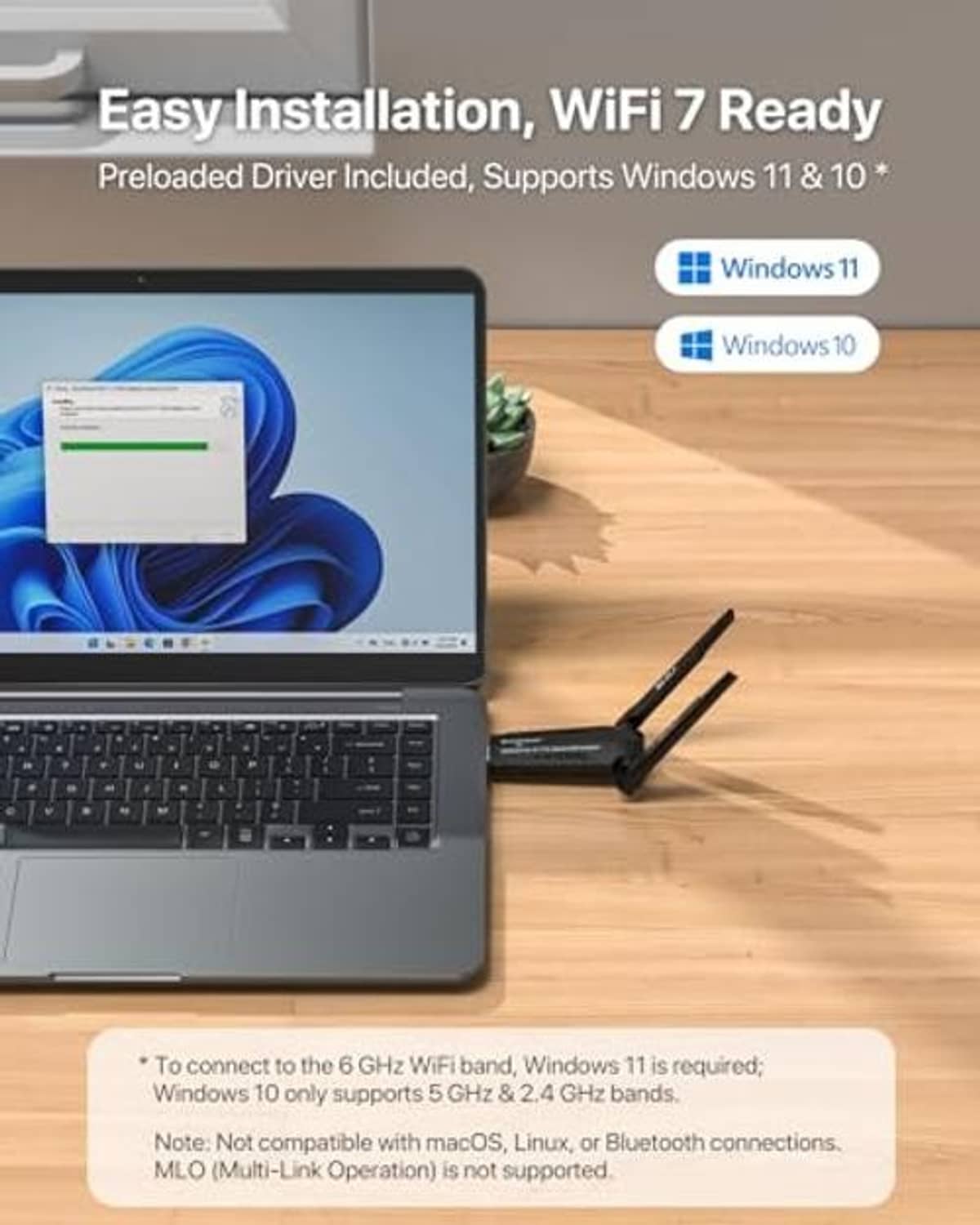 USB WiFi adapter on wooden desk beside laptop, two antennas extended.