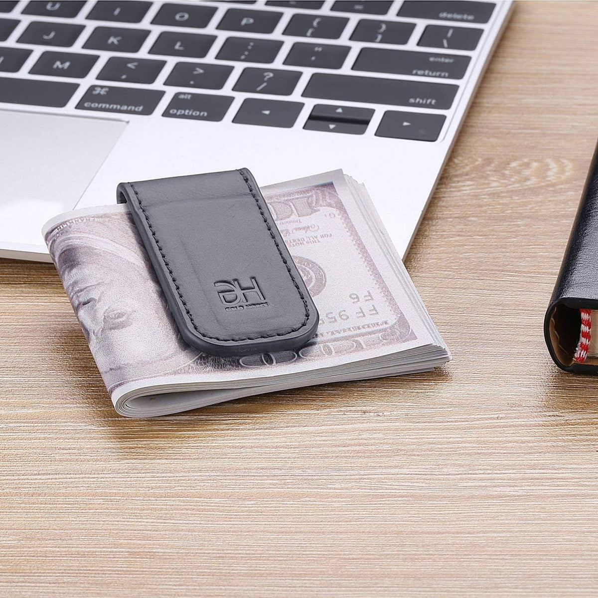 Grey genuine leather magnetic money clip with EH logo, holding folded bills on desk