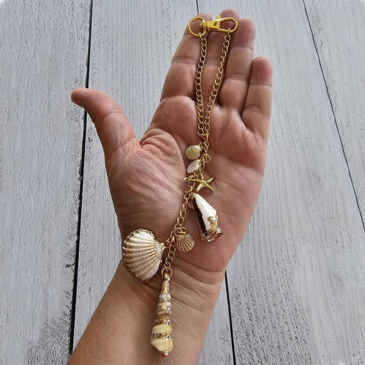 Sea shell charm on a gold chain with starfish, conch, and seashell pendants shown in hand