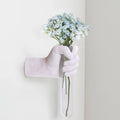 White hand vase wall hanging holding a bouquet of small white daisy-like flowers