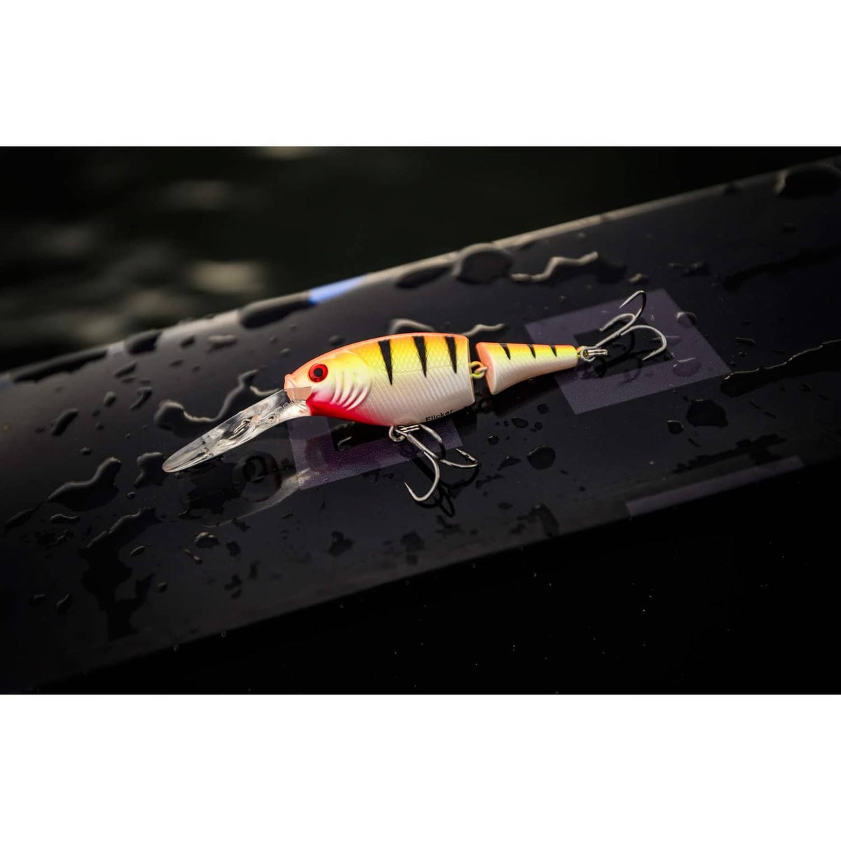 White and yellow crankbait lure with red stripes and treble hooks on dark tackle board