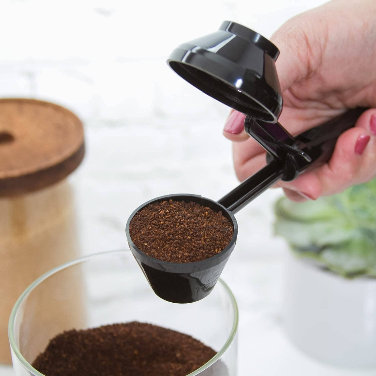 Black scoop pouring ground coffee into a purple reusable coffee pod cup