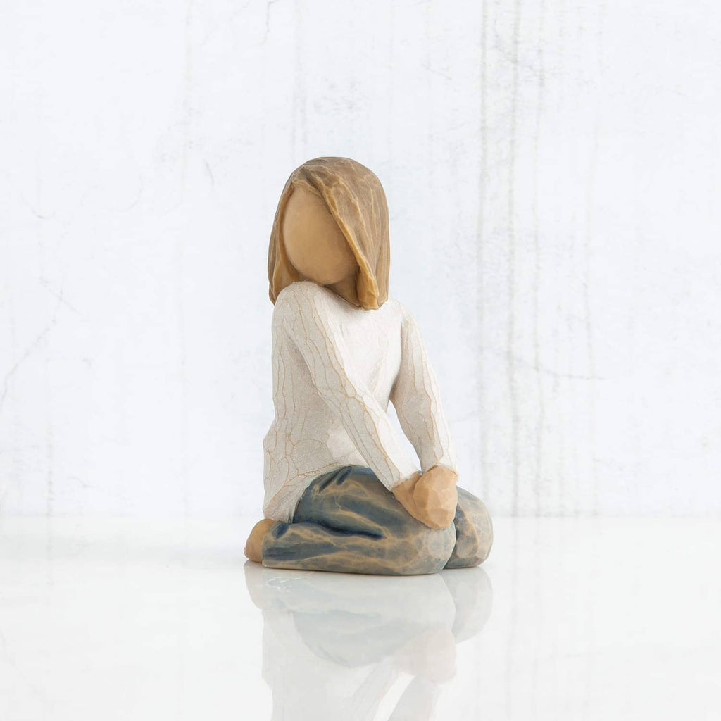 Kneeling child figurine in rear three-quarter view, white robe and blue-gray blanket.