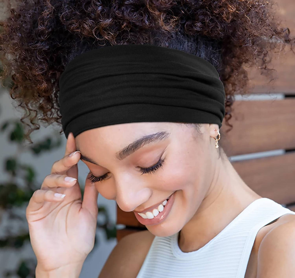 Wide elastic black headband worn on a curly hairstyle with smiling model.