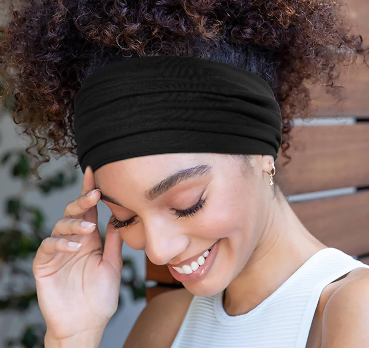 Wide elastic black headband worn on a curly hairstyle with smiling model.