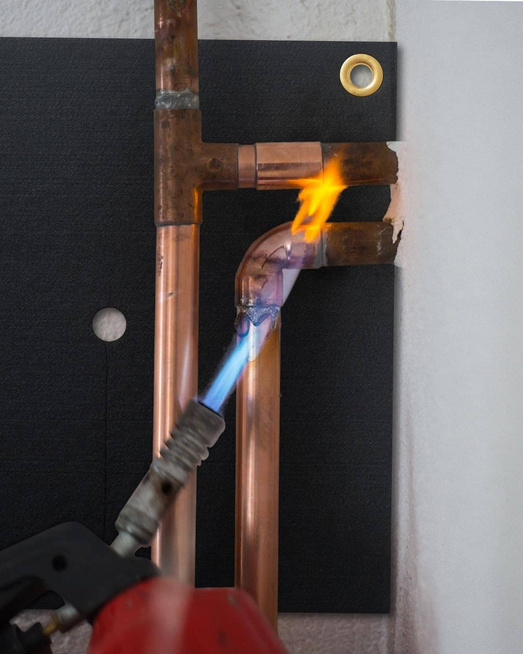 Black fireproof welding heat shield mat with grommets protecting copper pipes