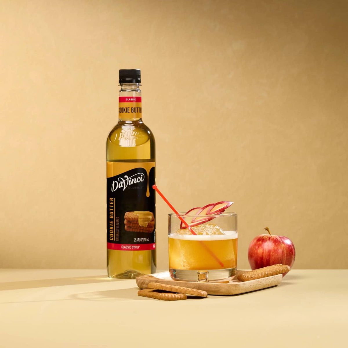 Cookie butter syrup bottle beside iced drink in glass with cookies and apple