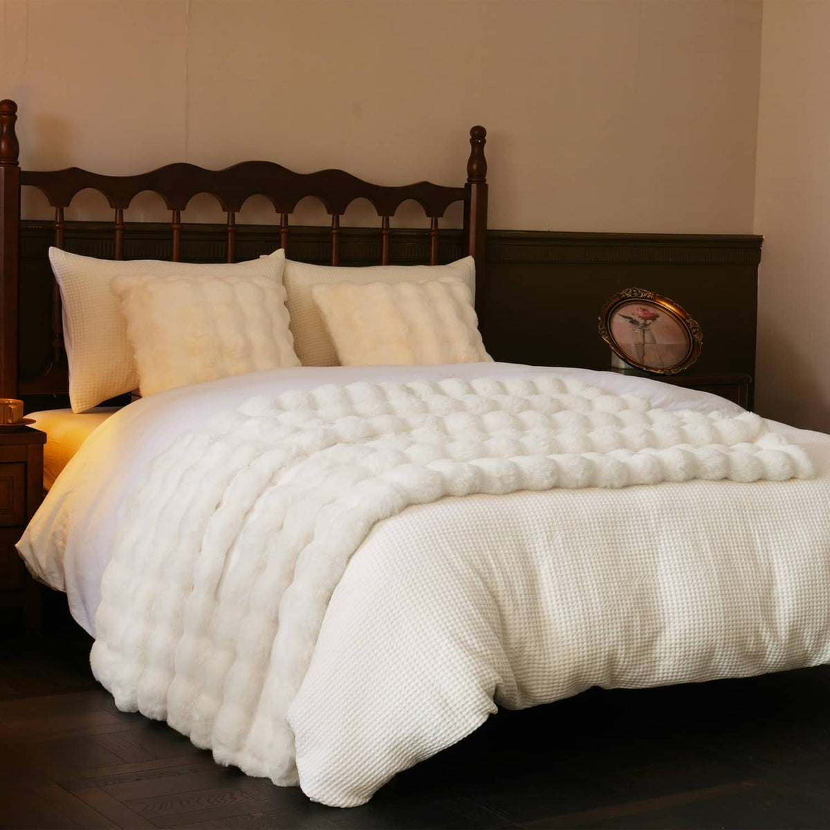 Cream faux fur throw blanket folded on a bed over a light duvet