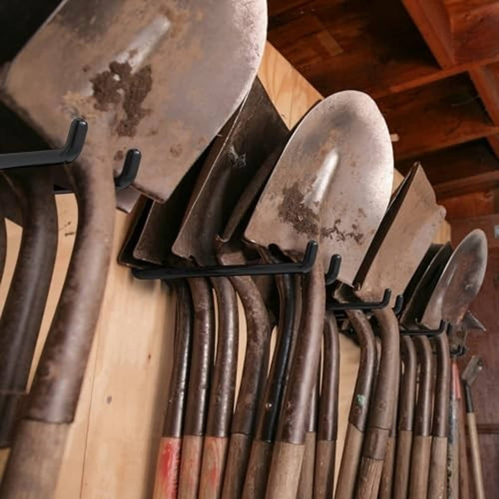 Black garage wall hooks holding long-handled tools like shovels and rakes