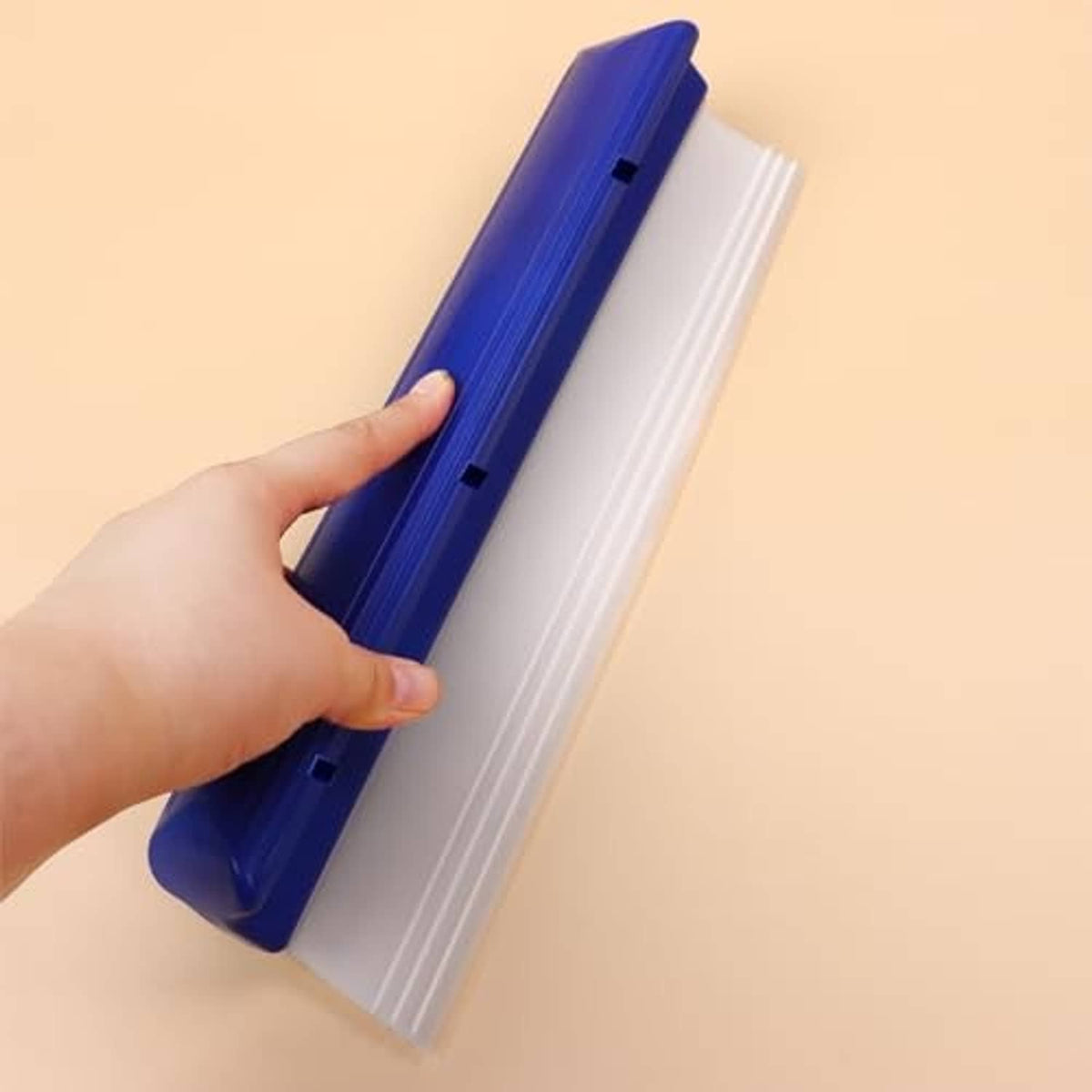 Hand holding blue handle and white blade car drying squeegee on smooth surface
