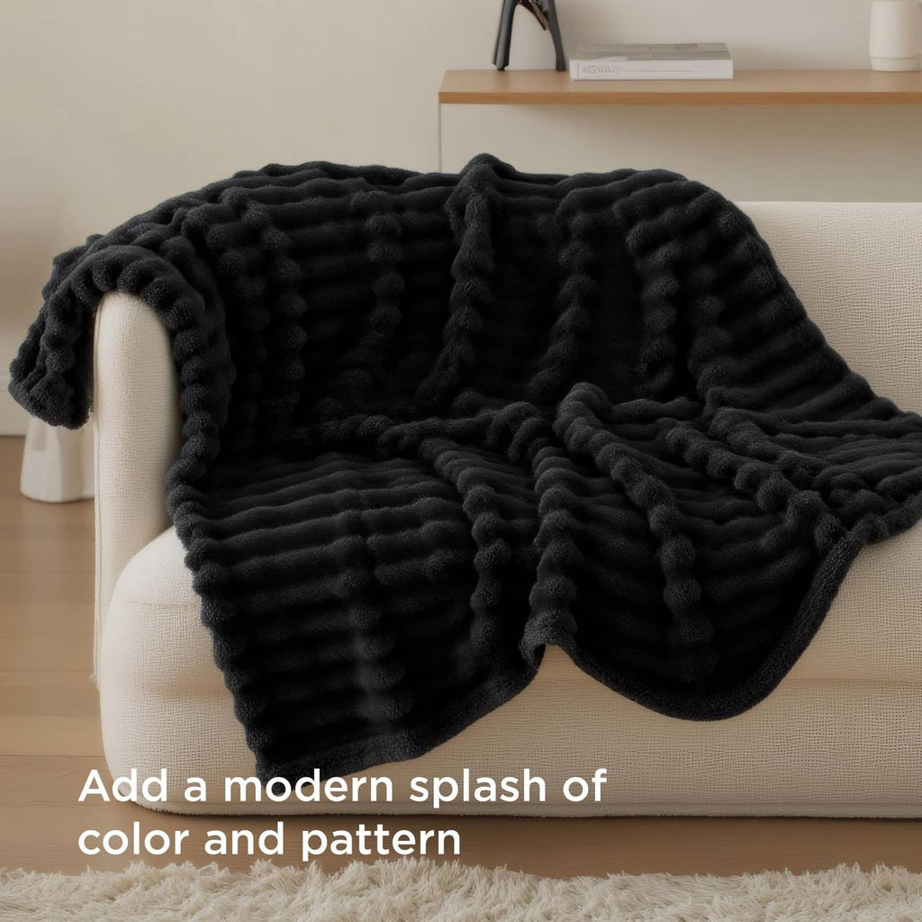 Black chunky-knit throw blanket draped over a light sofa arm