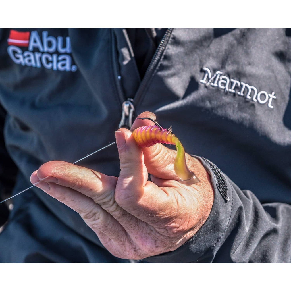 Orange-pink soft plastic fishing grub bait with curled segmented body held in hand