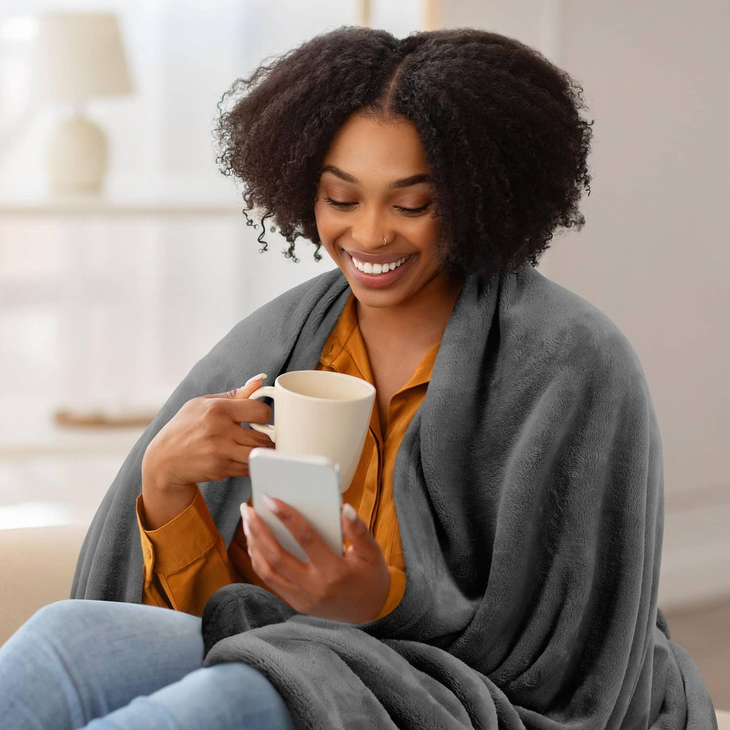 Grey fleece blanket wrapped around a person holding a mug indoors.