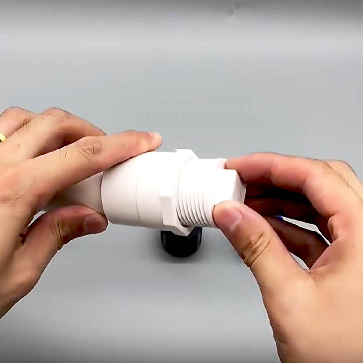 Hands fitting a white PVC threaded plug cap onto a pipe end