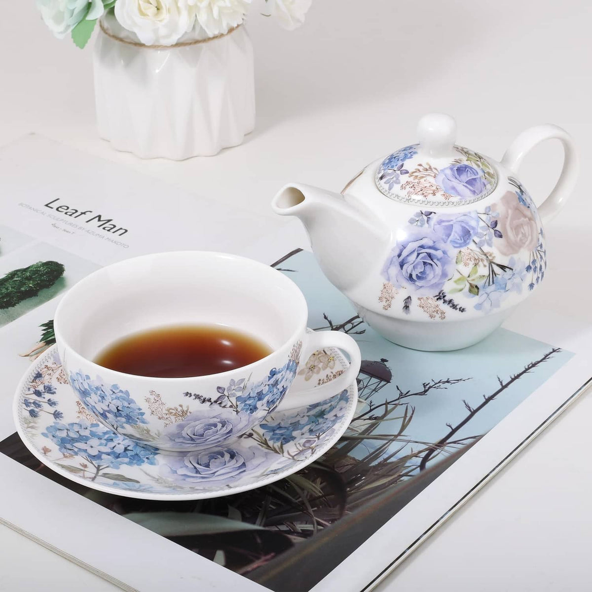 Porcelain tea for one set with blue rose teacup and teapot on patterned tray.