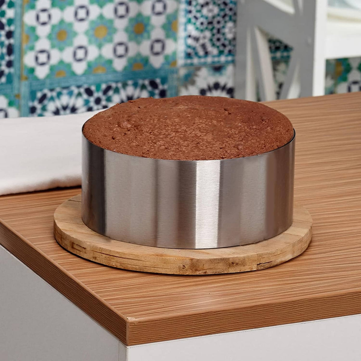 Stainless steel round cake ring around a chocolate cake layer on a wooden base