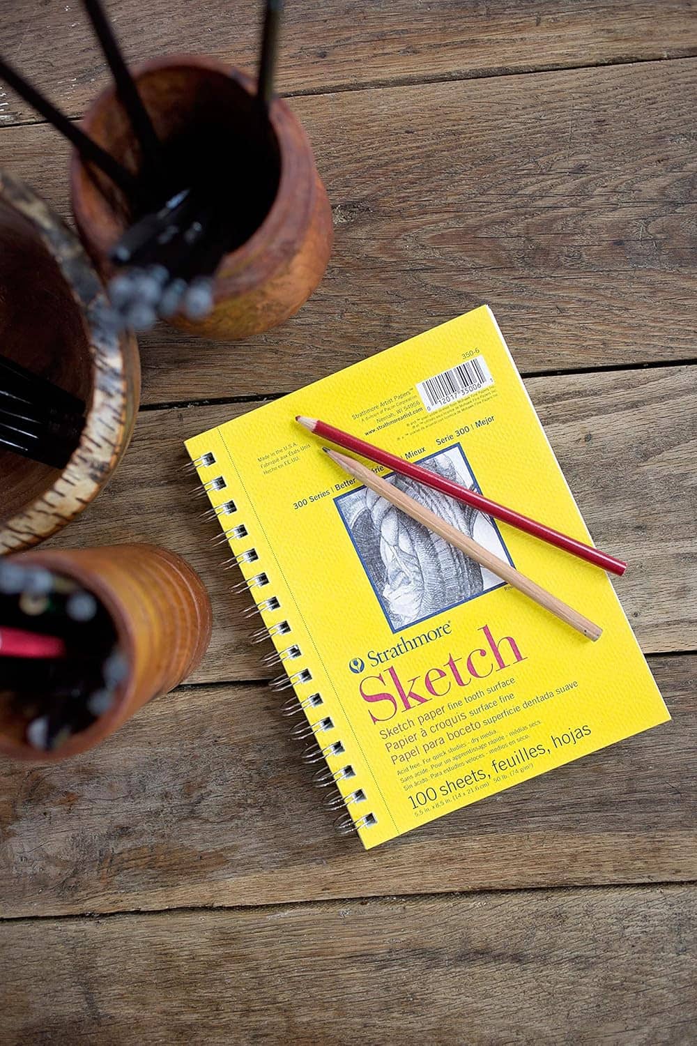 Yellow spiral sketch pad on wooden surface with pencils and art tools