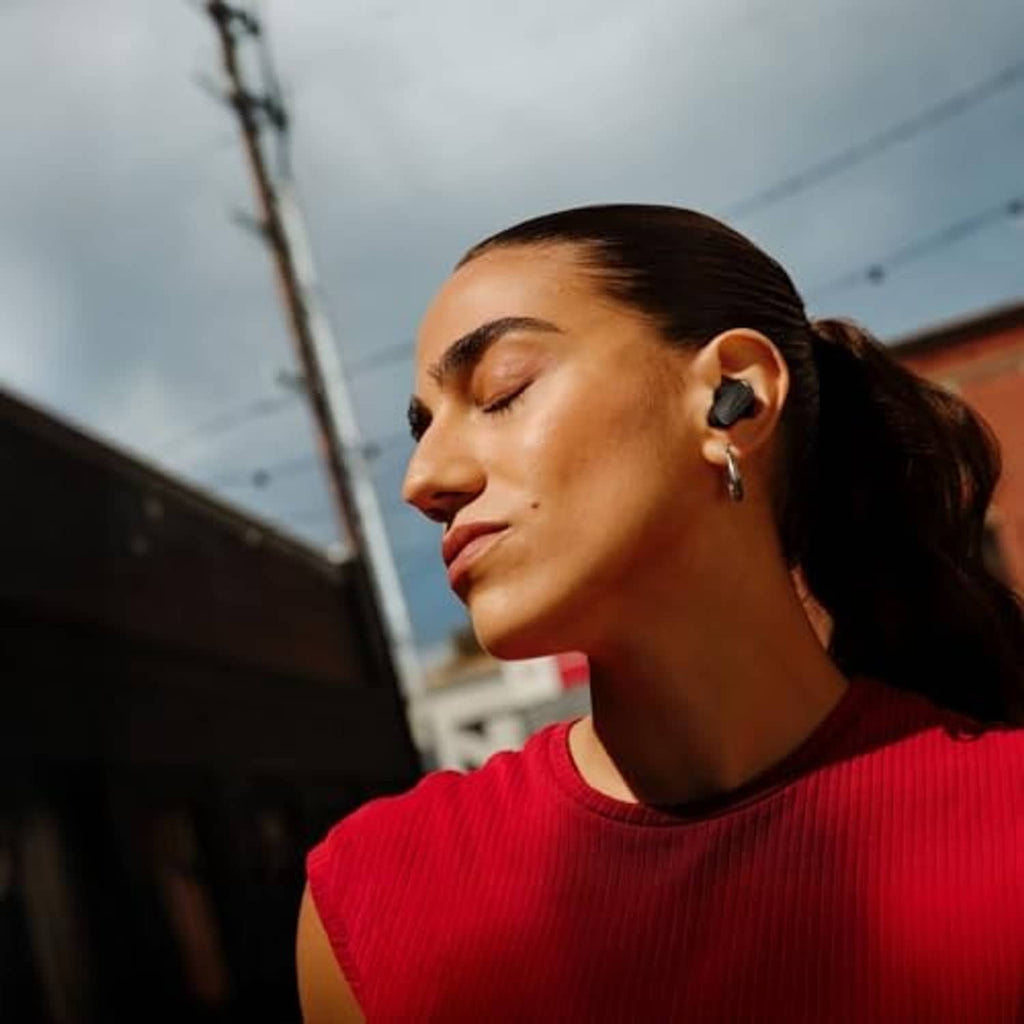 Black wireless earbuds in a woman's ear with small ear fins for secure fit