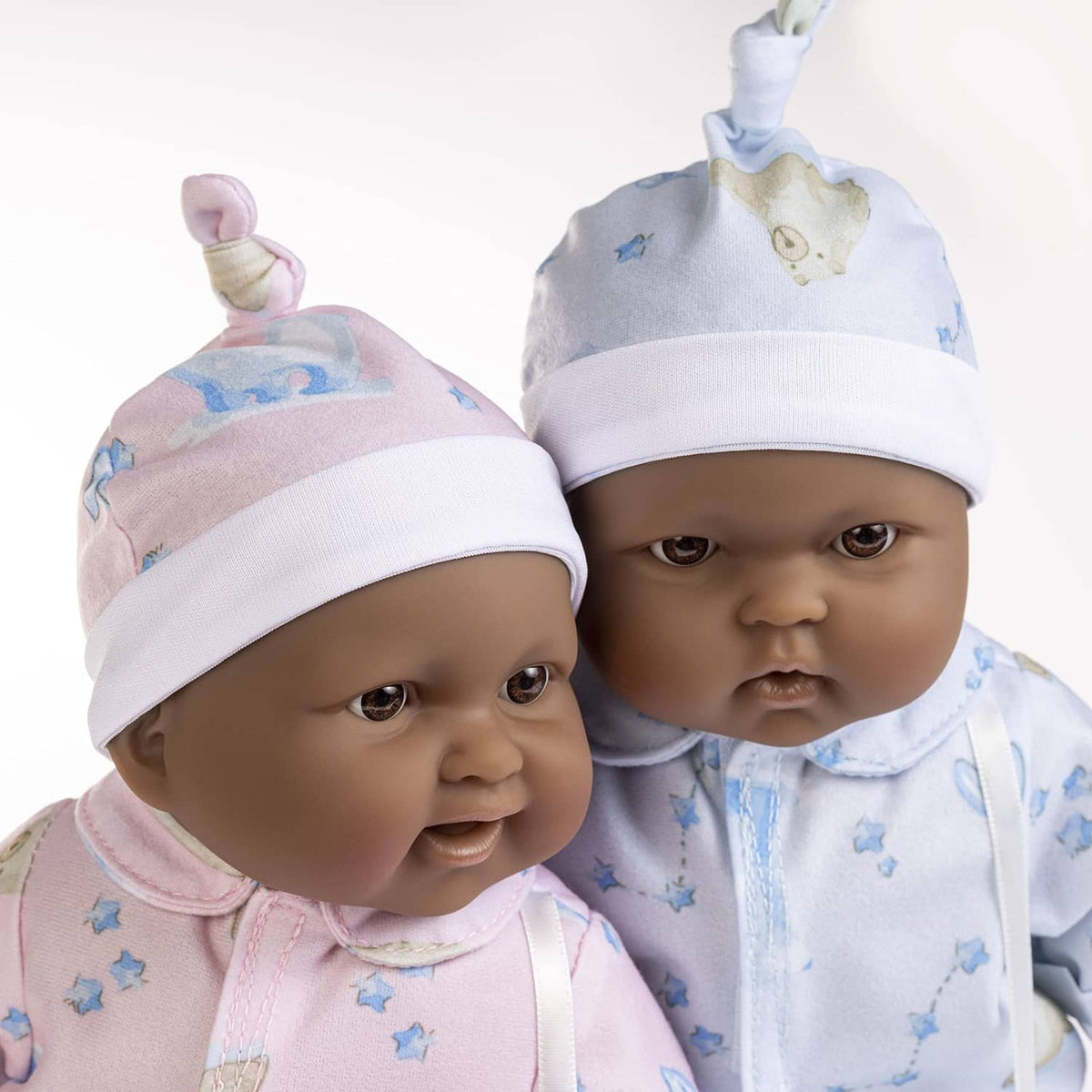 Close-up of twin soft body baby dolls wearing pink and blue patterned caps
