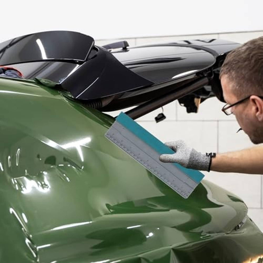 Hand holds teal-and-gray vinyl squeegee for smoothing car window tint film