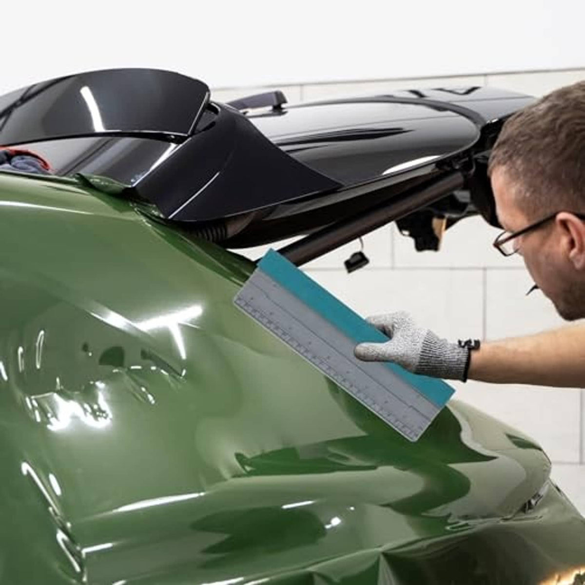 Hand holds teal-and-gray vinyl squeegee for smoothing car window tint film