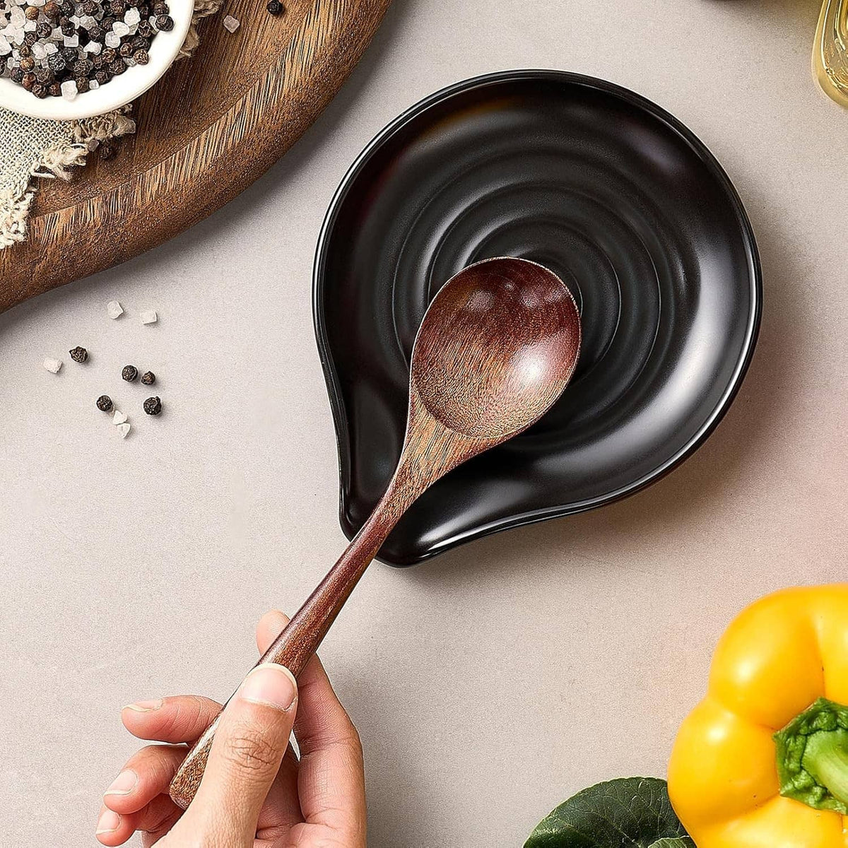 Black spoon rest with concentric pattern and wooden spoon in a hand