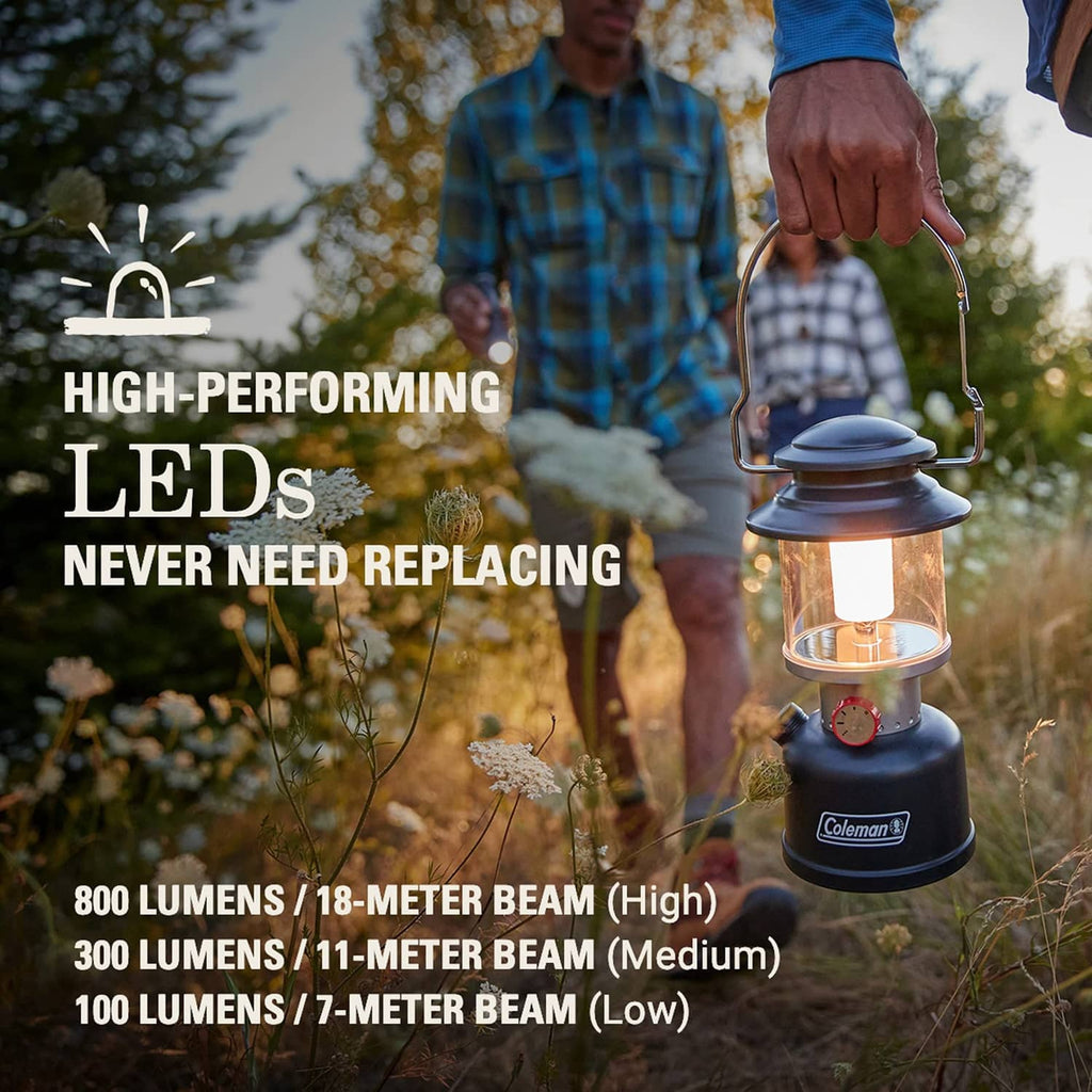 Black Coleman LED lantern in hand with clear top lens and metal carry handle.
