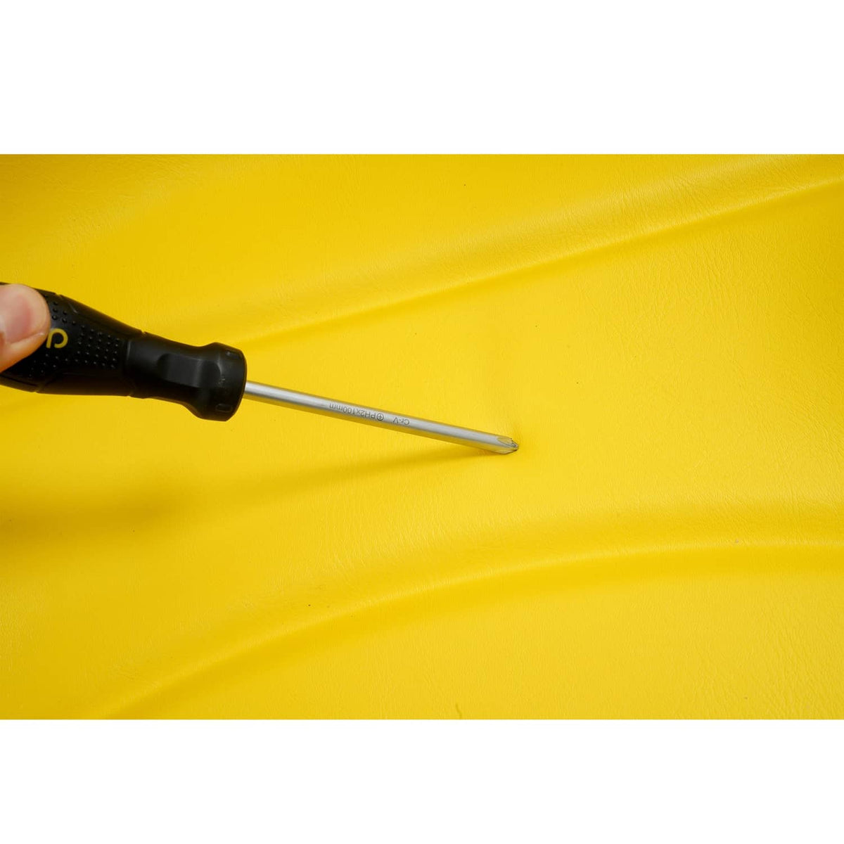Tractor seat cushion with screwdriver tip poised on yellow upholstery