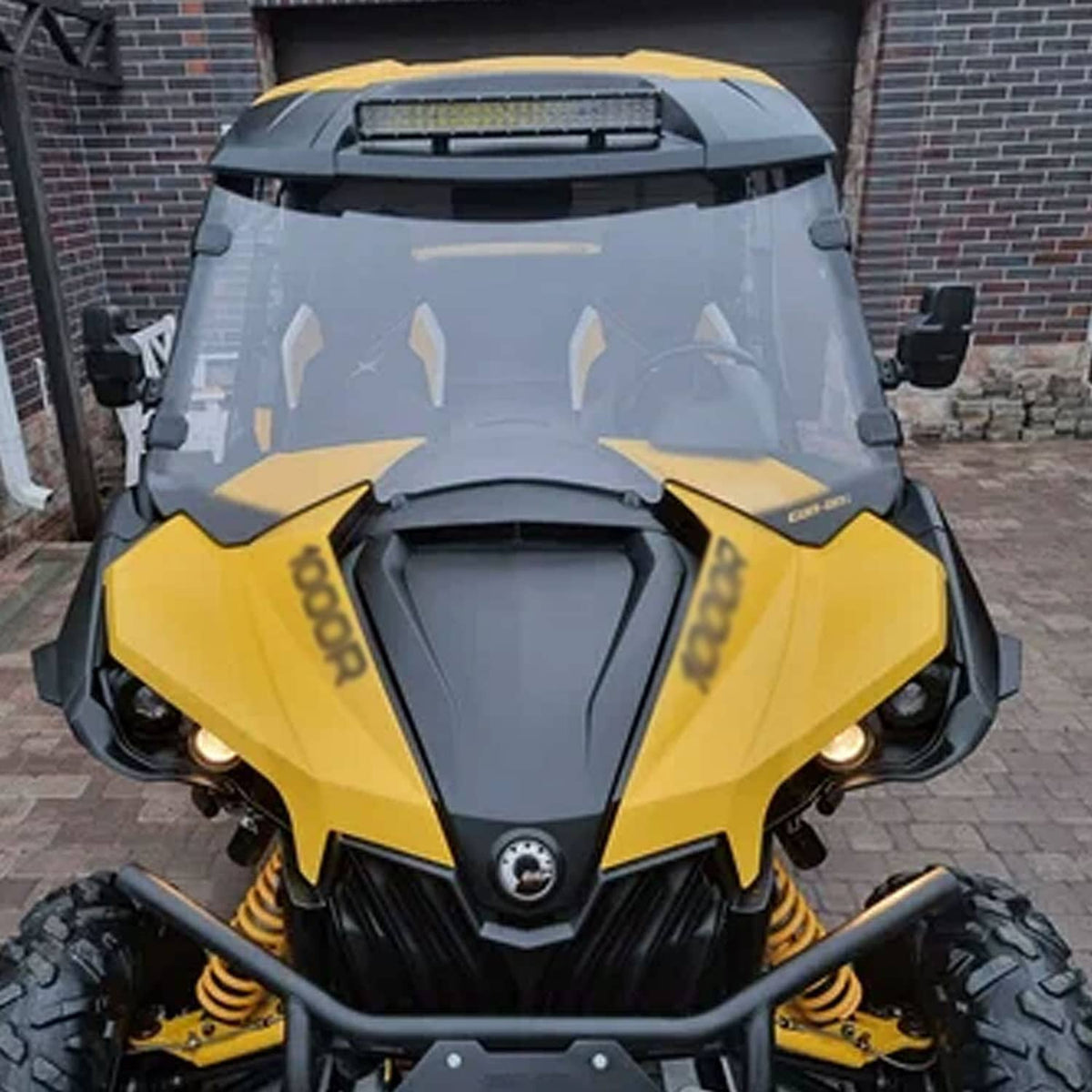Clear UTV windshield panel with black side brackets on a yellow off-road vehicle