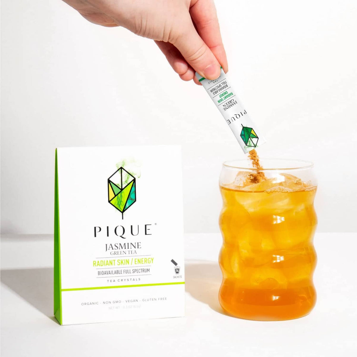 Hand pouring tea crystals sachet into a glass of jasmine green tea